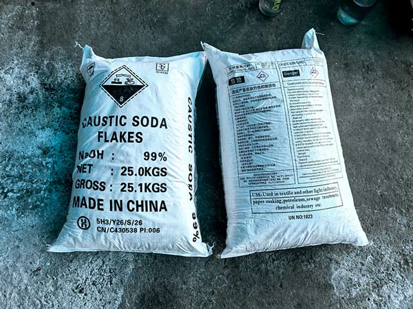 Factory worker guiding 25kg bag of caustic flakes through automated heat sealing machine