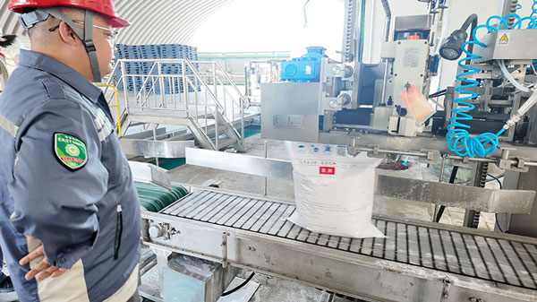 Plant supervisor with hard hat monitoring the automated bagging process for caustic pearl