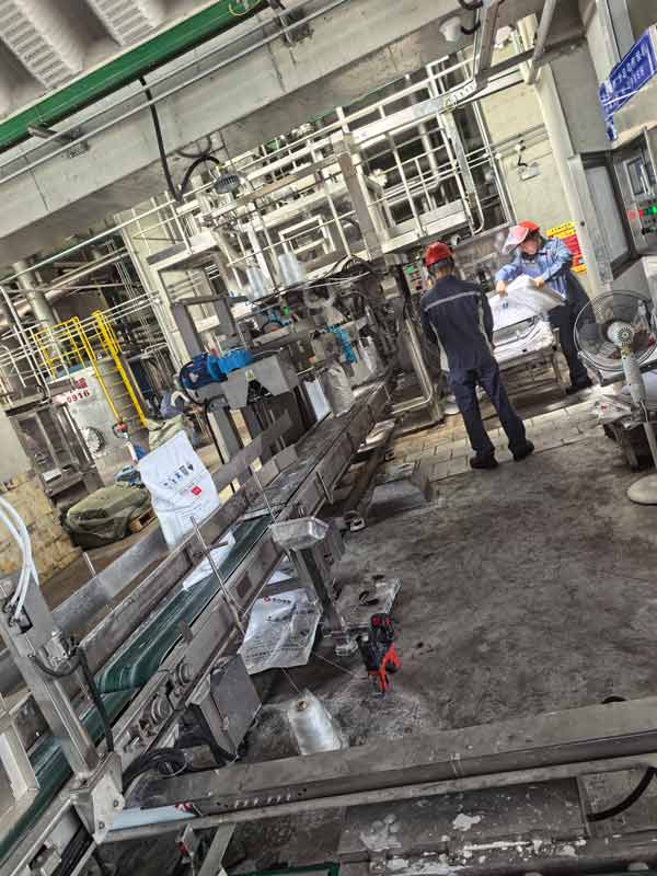 Chemical plant worker checking pressure gauges along caustic soda flakes liquid reaction line