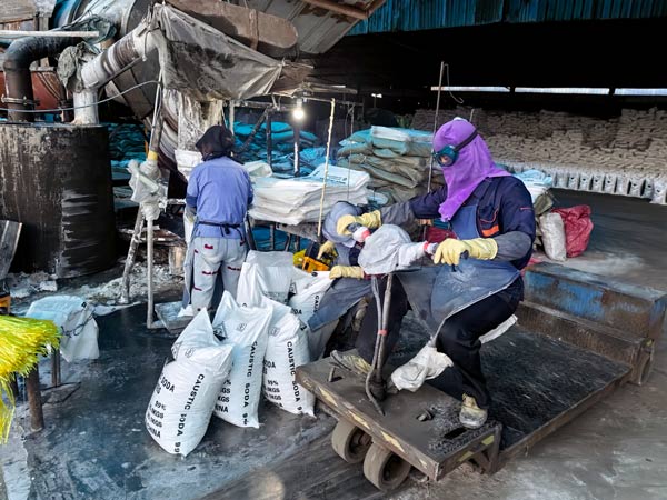 Packaging operator wearing heavy duty nitrile gloves securing a 25 kg bag of caustic soda pearls 99