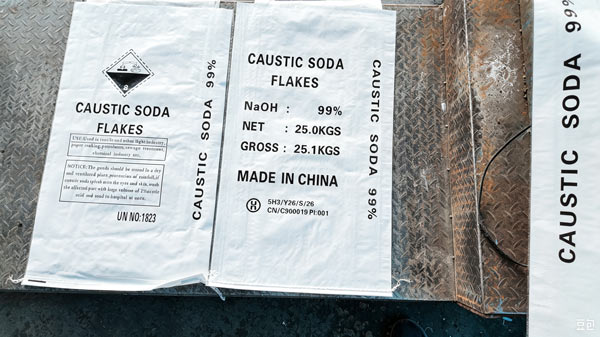 Waterproof plastic underlay sheet positioned on wooden pallet base beneath GACL caustic soda flakes bags