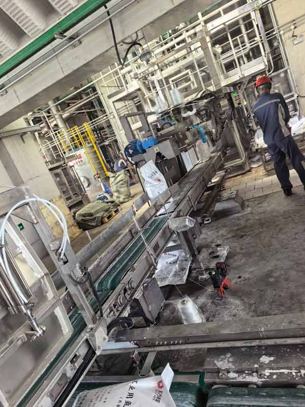 Packaging technician monitoring automated heavy duty sewing head stitching Grasim caustic soda flakes 25kg bags