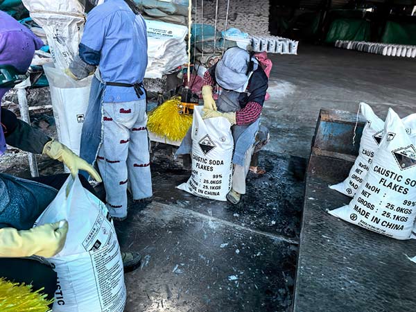 Plant worker operating handheld bag stitching machine to seal top of soda flakes package