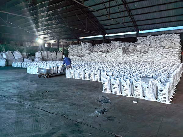 Wide shot of a massive industrial warehouse filled with hundreds of stacked caustic soda flakes bags
