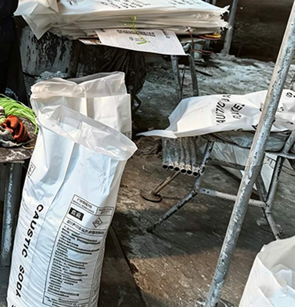 Close up of flexible woven hanging tag displaying bold English product name on a caustic soda flakes sodium hydroxide bulk bag