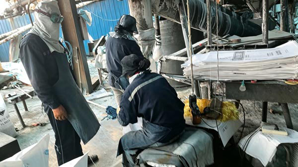 Factory worker operating pneumatic filling spout to load sodium hydroxide flakes for soap making into multiwall packages