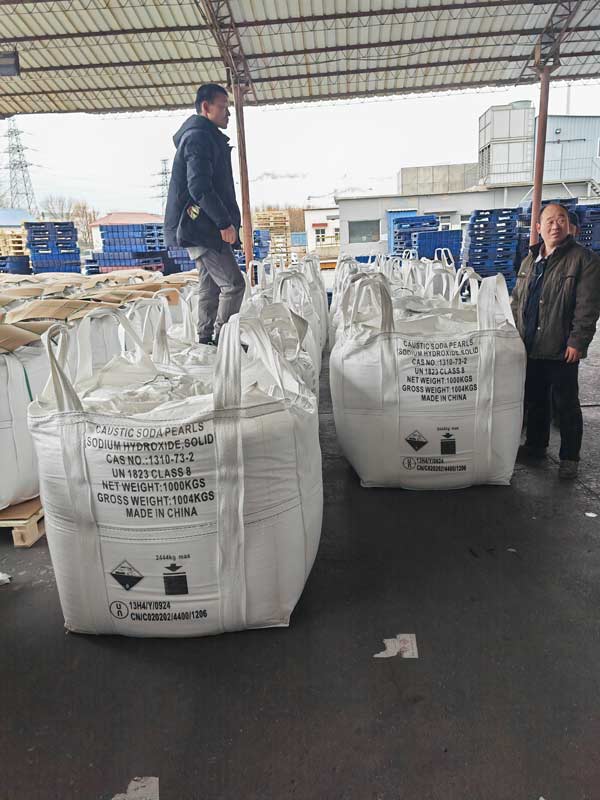 Warehouse staff standing beside stacked acid caustic soda pearls ton bags ready for container freight loading