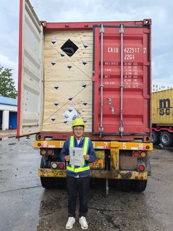 Inspector in high-visibility vest standing in front of a shipping container loaded with market grade caustic soda pearls