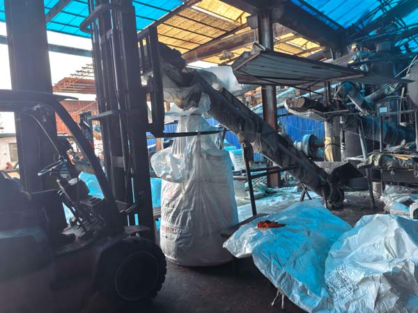 Forklift truck lifting heavy bulk jumbo bag near processing equipment during caustic soda pure manufacturing