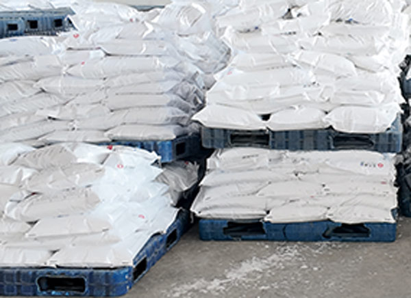 Clean white caustic soda supply bags neatly stacked on blue plastic pallets inside a spacious warehouse
