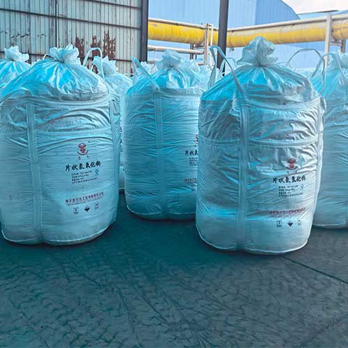 Bulk jumbo bags of raw sodium hydroxide stored at a factory, used in formulating industrial cleaning products with sodium hydroxide.