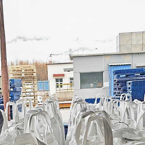 Outdoor chemical storage area showing bulk FIBC tote bags of NaOH sodium staged for international freight shipping.