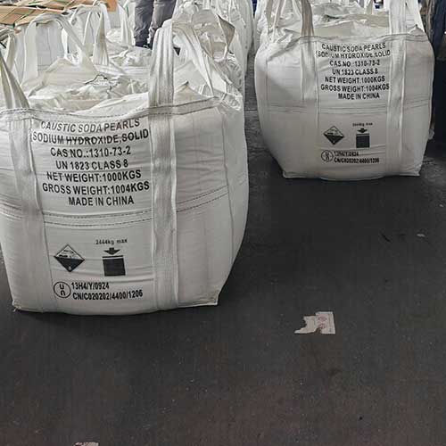 Large 1000kg FIBC bulk bags of caustic soda pearls labeled with UN 1823 Class 8 hazardous chemical specifications.