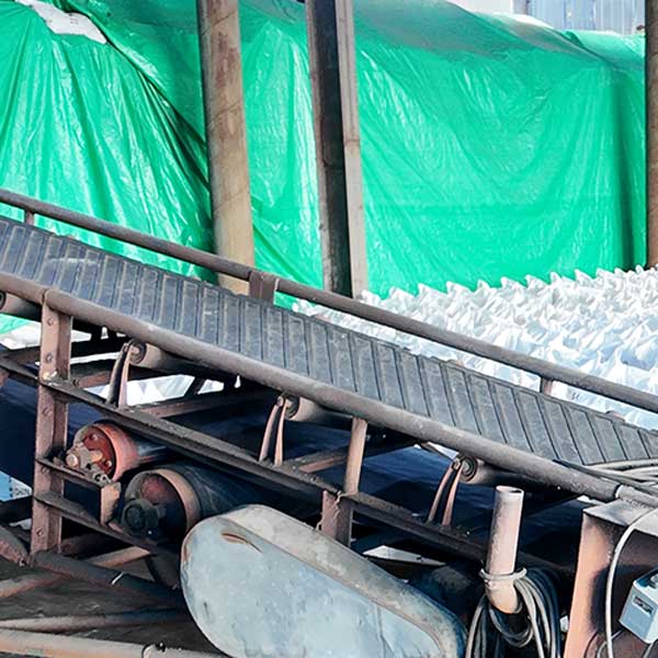 Industrial belt conveyor system handling bagged Sodium Hydroxide NaOH for high-volume beryllium extraction.