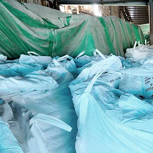 large chemical warehouse stacked with neat rows of white sodium hydroxide 99 bags alongside bulk FIBC jumbo bags.