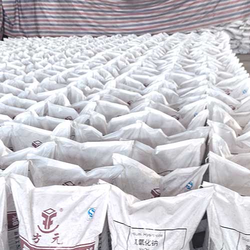 Extensive rows of 25kg moisture-proof woven bags filled with high-purity caustic prills in a factory warehouse