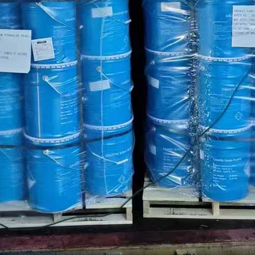 Stacked blue metal drums on sturdy wooden pallets, packed for safe transport of sodium hydroxide beads.