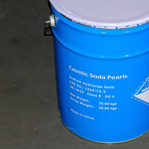 Sealed blue steel drum stored on concrete workshop flooring, ready for global shipping of sodium hydroxide prills.