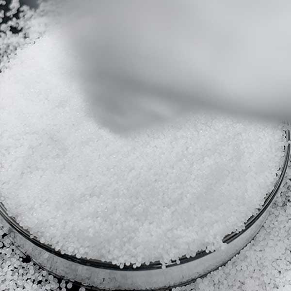 Free-flowing 99% pure white prills displayed in a laboratory glass dish from certified caustic soda prills manufacturers.