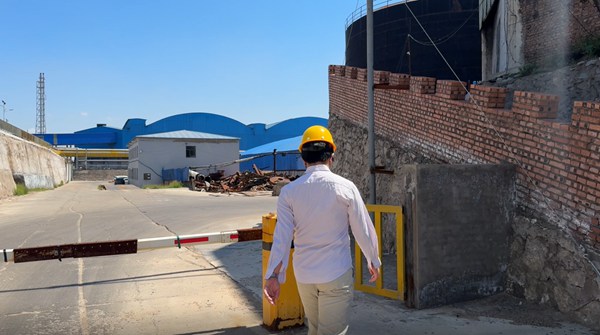 Operations supervisor conducting site walk-through along industrial access road of caustic soda 98 factory complex.